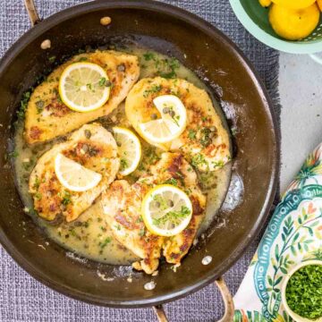 Chicken piccata in a saute pan with lemon slices.