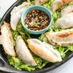 gyoza sauce in a blue bowl surrounded by potstickers