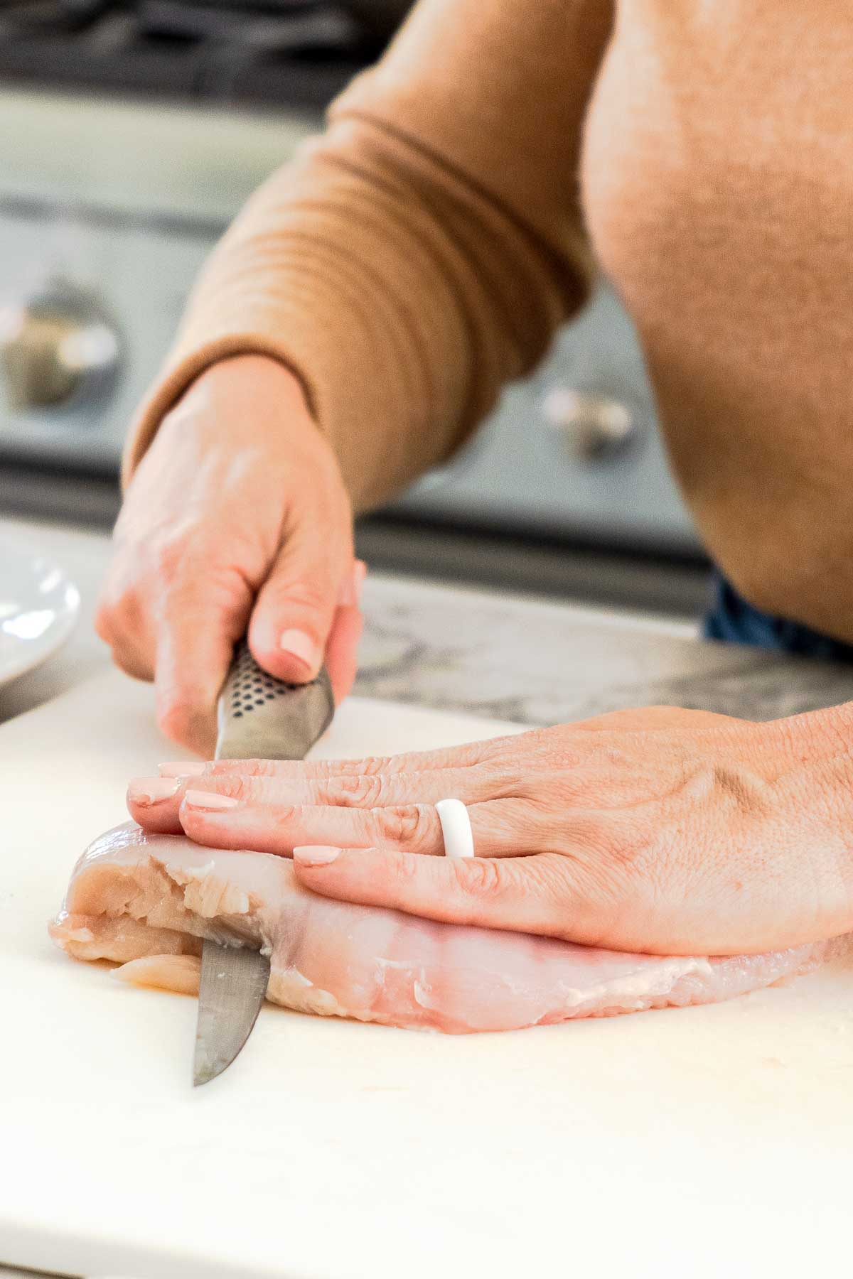 Person cutting chicken breast into fillets with a knife.