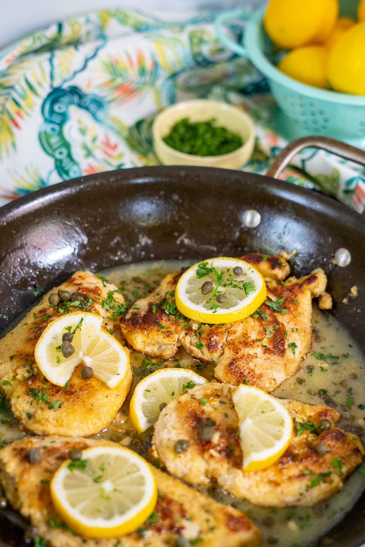 Chicken piccata in skillet with sauce, fresh parsley, and lemon slices for garnish. 