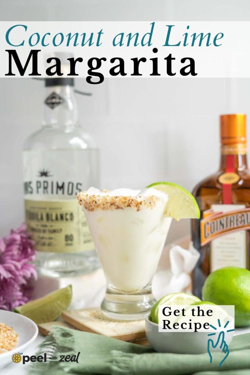 A coconut margarita with lime in a glass with a toasted rim, garnished with a lime wedge, sits in front of tequila and Cointreau bottles with limes nearby.