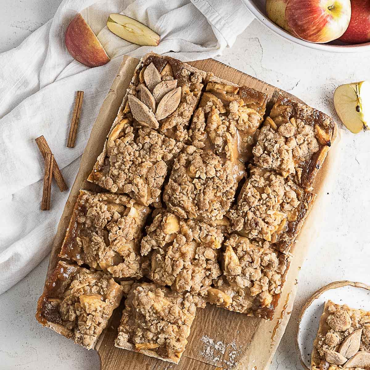 A batch of apple crumble bars made with oat flour, cut into squares on a wooden board, with apple slices and cinnamon sticks nearby—a delicious treat for fans of oat flour recipes.