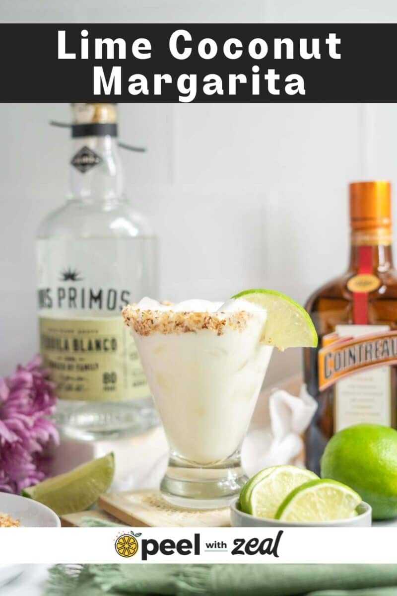 A coconut margarita in a glass with a toasted rim, garnished with a lime wedge, sits before tequila and Cointreau bottles, surrounded by sliced limes.