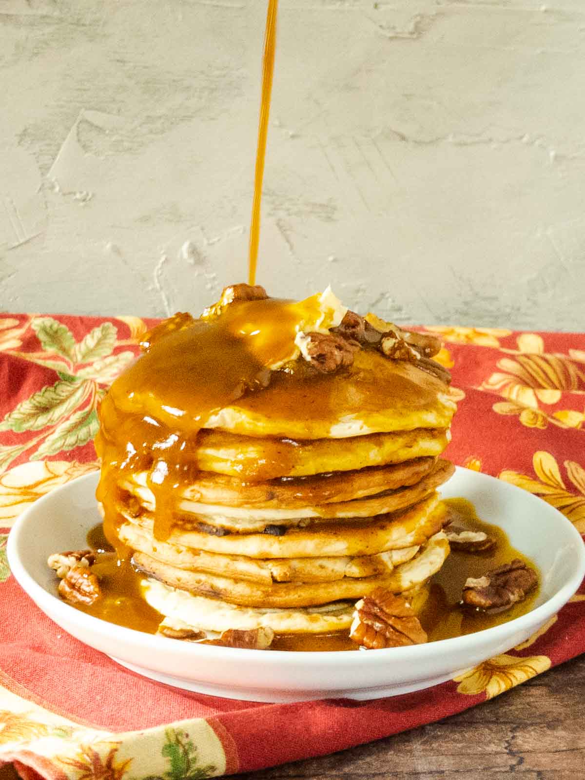 syrup being poured over a stack of pumpkin pancakes