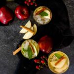 apples and cinnamon sticks with whiskey cocktail on black background