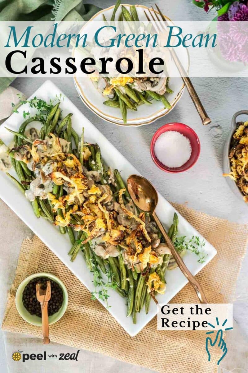 Overhead view of modern green bean casserole topped with crispy onions on a rectangular platter, surrounded by serving utensils and small bowls with ingredients.
