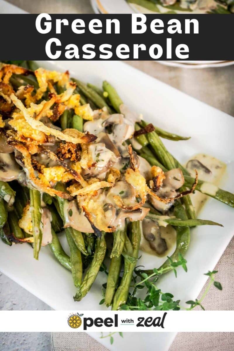 A plate of modern green bean casserole topped with crispy onions and sliced mushrooms, served on a white dish with a sprig of fresh herbs.