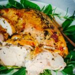roasted turkey breast carved and on a platter with fresh herbs