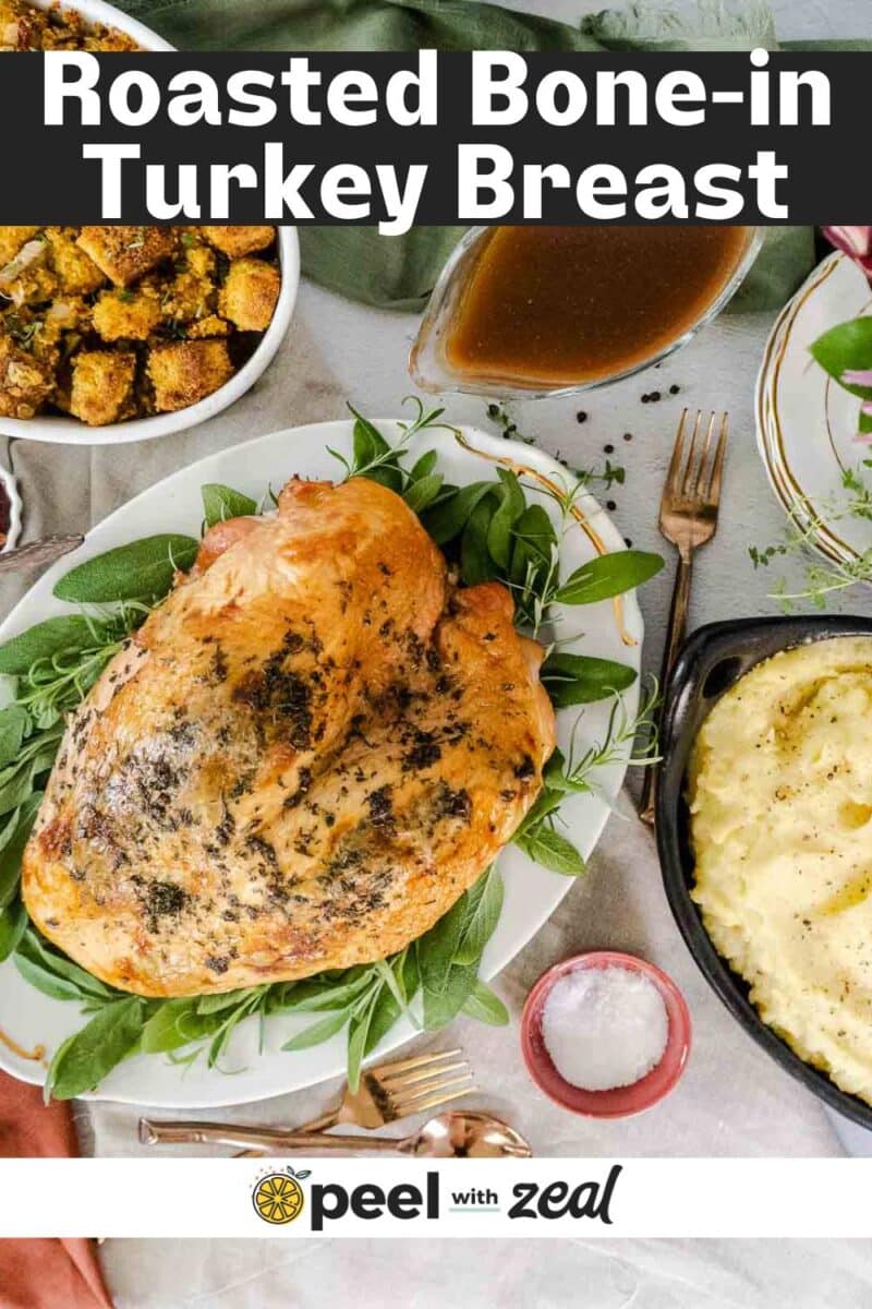 A roasted bone in turkey breast on a platter with fresh herbs, surrounded by creamy mashed potatoes, savory stuffing, rich gravy, and a small bowl of salt on a white tablecloth.