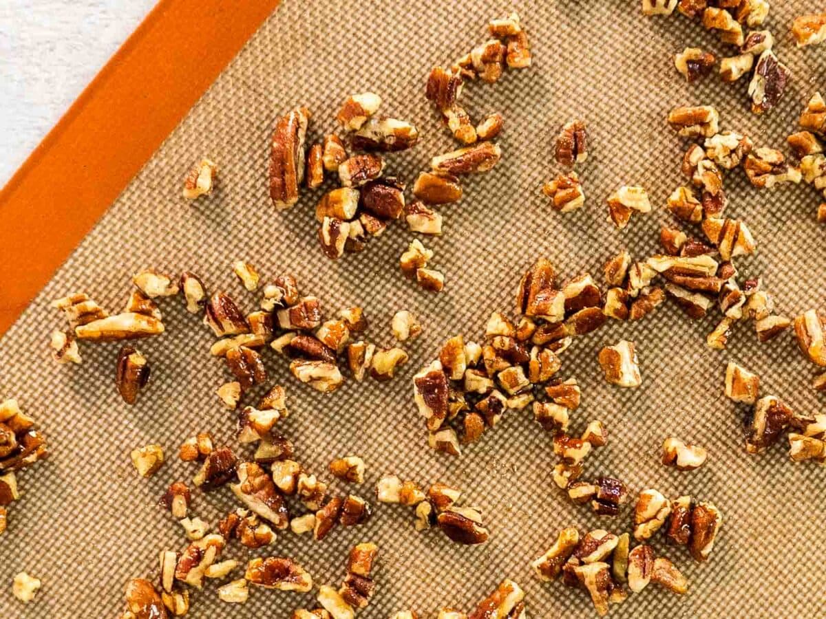 Chopped pecans spread out on a silicone baking mat, ready for toasting-perfect as a crunchy topping for maple creme brulee.
