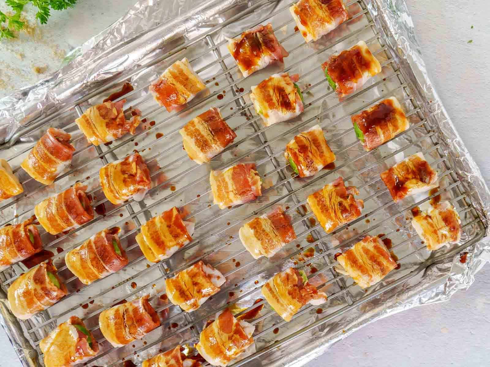 Bacon-wrapped Brussels sprouts rest on a wire rack over foil, evenly spaced and glazed with sauce.