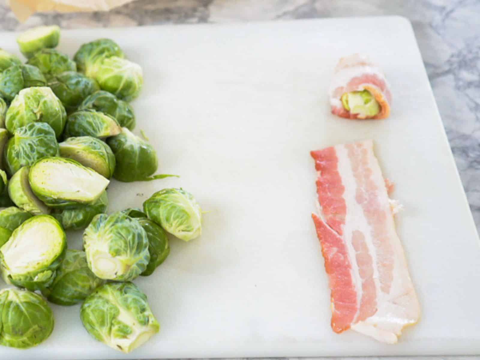 Brussels sprouts sit neatly on a cutting board, with one beautifully transformed into a bacon-wrapped delight.