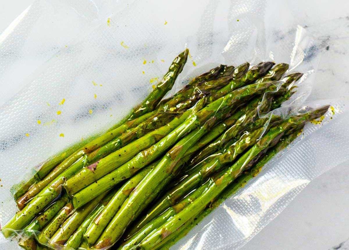 Fresh sous vide asparagus spears vacuum-sealed in a clear plastic bag, resting on a white surface.