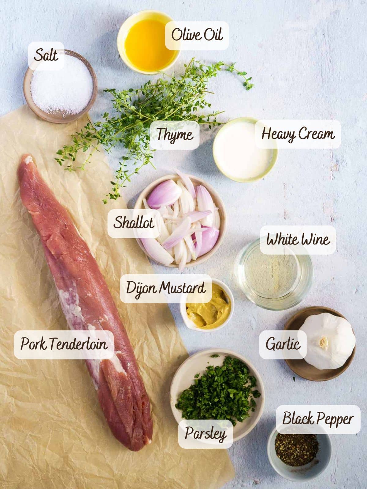 Uncooked sous vide pork tenderloin on parchment paper, surrounded by small bowls of salt, olive oil, thyme, heavy cream, shallot, white wine, Dijon mustard, garlic, parsley, and black pepper.