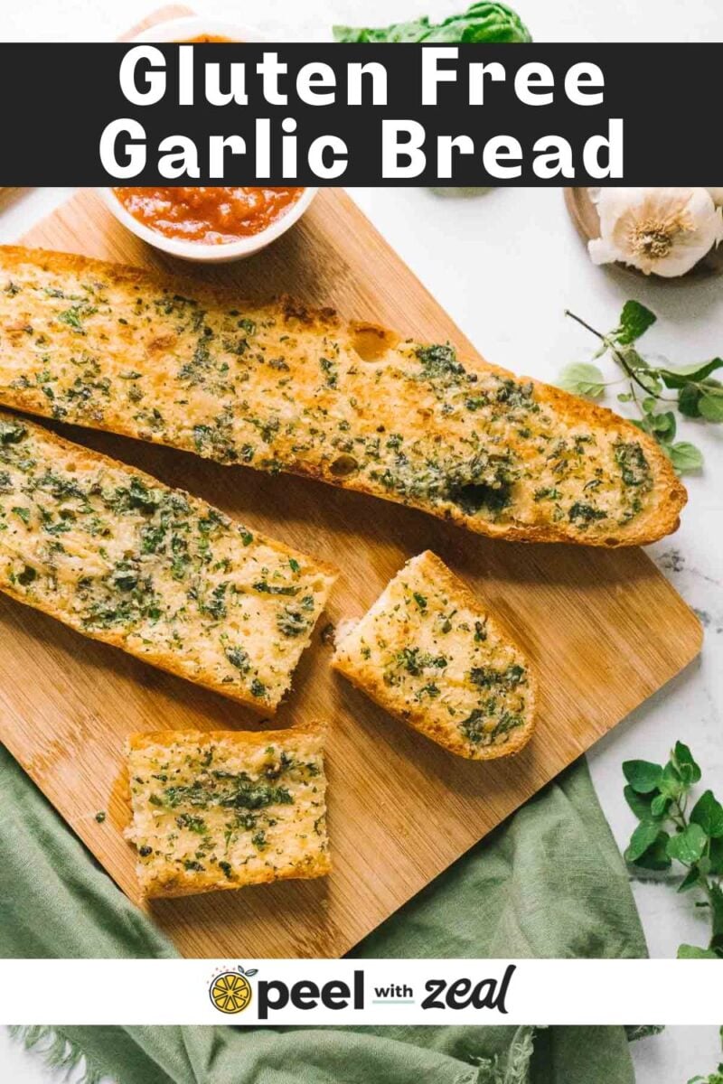 Sliced gluten free garlic bread on a wooden board with a small bowl of red dipping sauce, fresh herbs, and a garlic bulb nearby for the perfect savory snack.