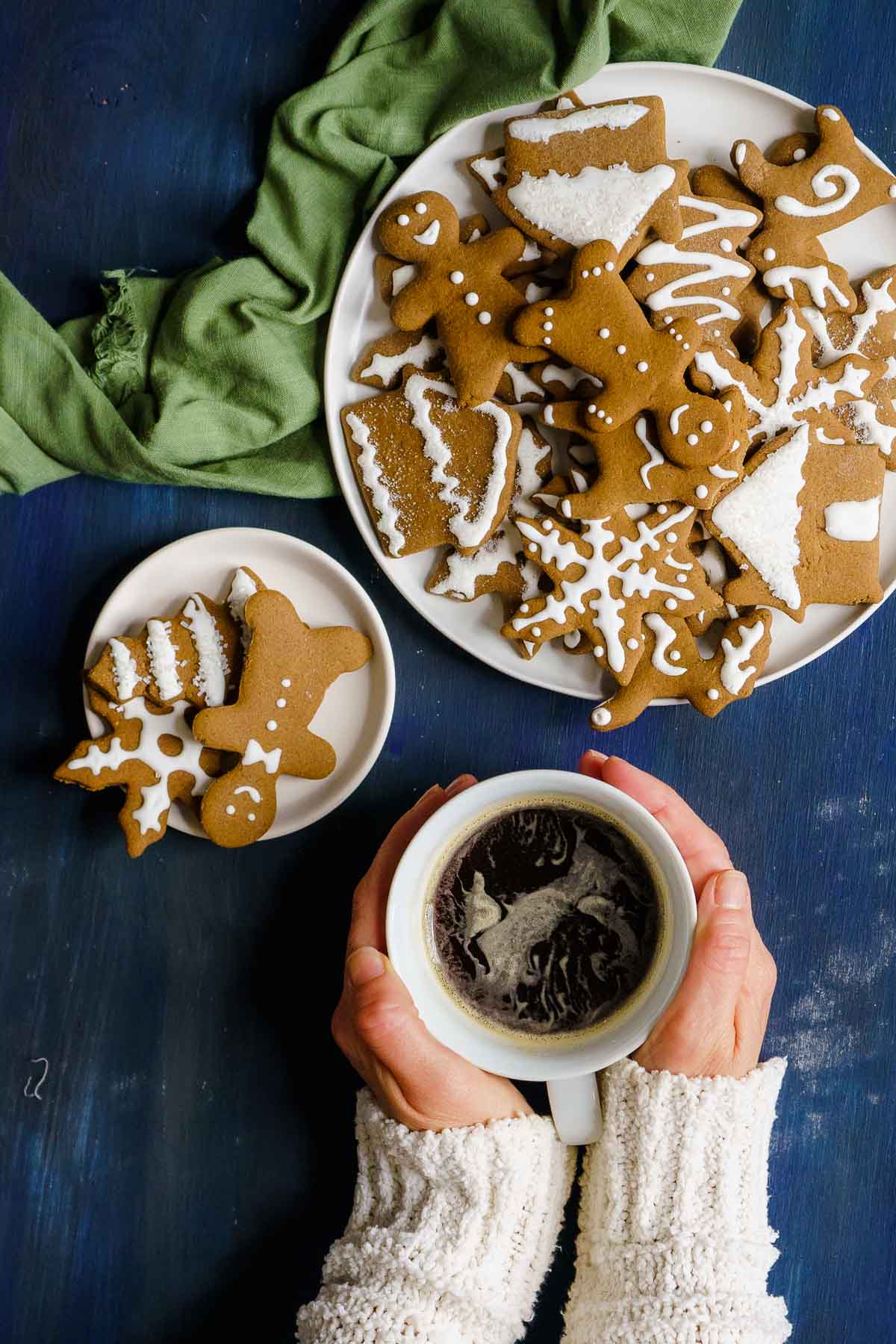 person holding coffee mug next to plate of gingerbread