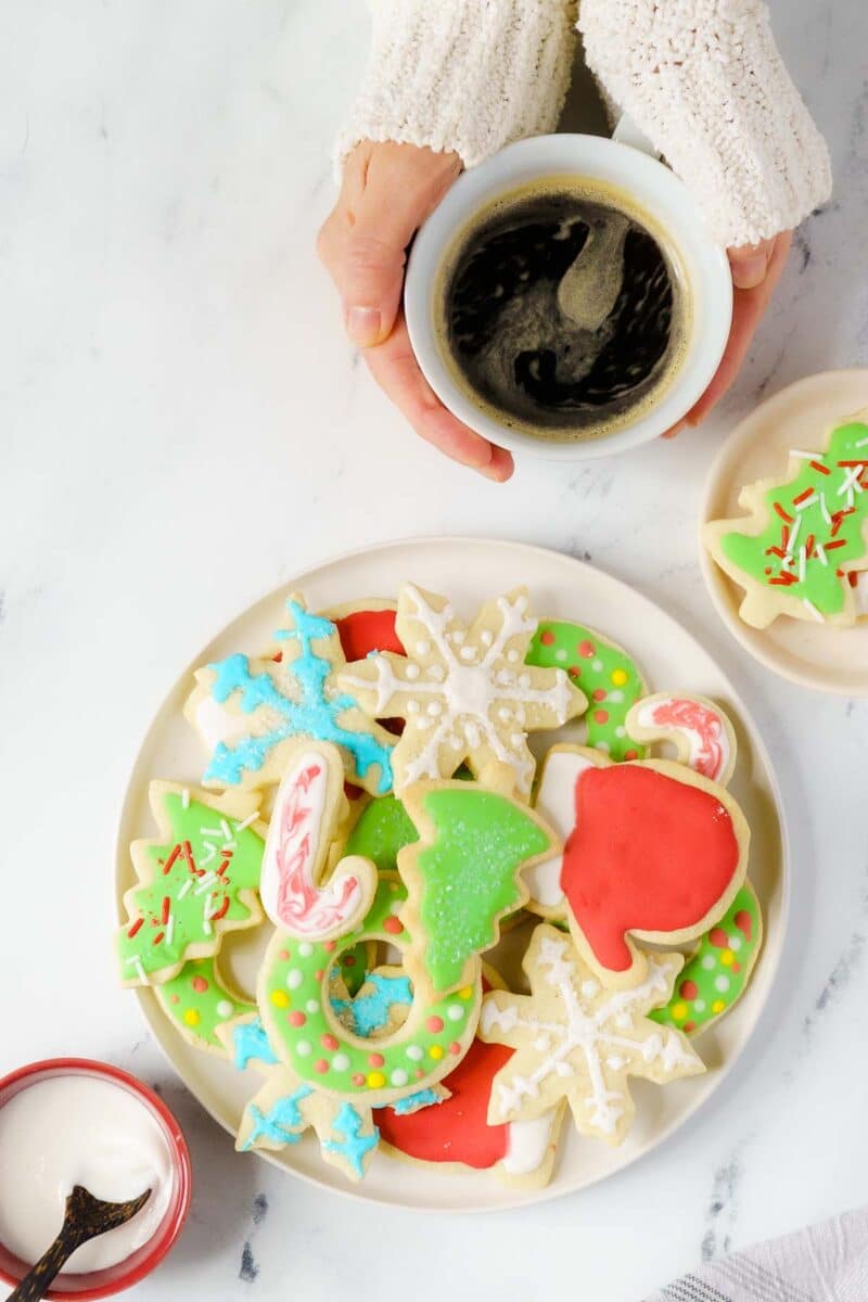 person holding cofee mug next to a plate of cookies