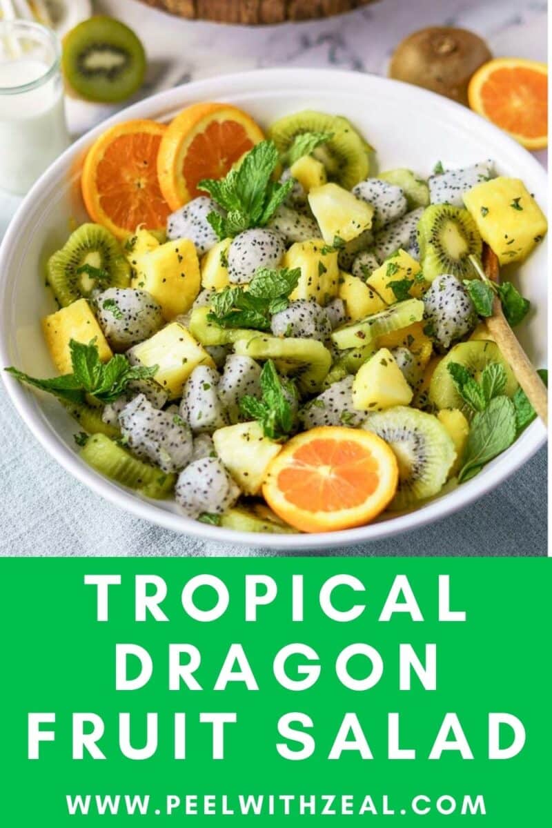 A bowl of refreshing dragon fruit salad featuring kiwi, pineapple, and orange slices, garnished with mint leaves and served with a wooden spoon.