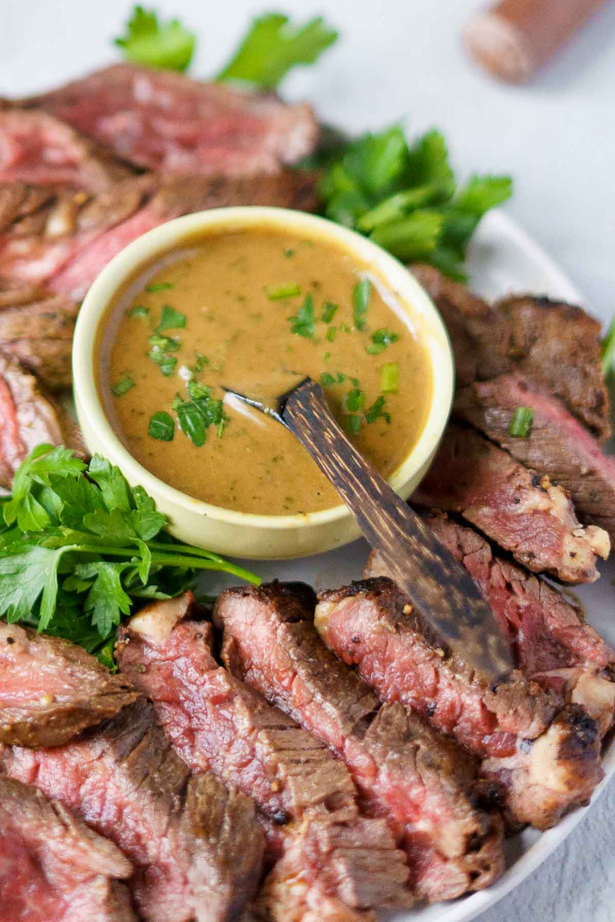 Sliced medium-rare bavette steak arranged around a bowl of brown sauce, garnished with fresh parsley, with a spoon in the sauce.