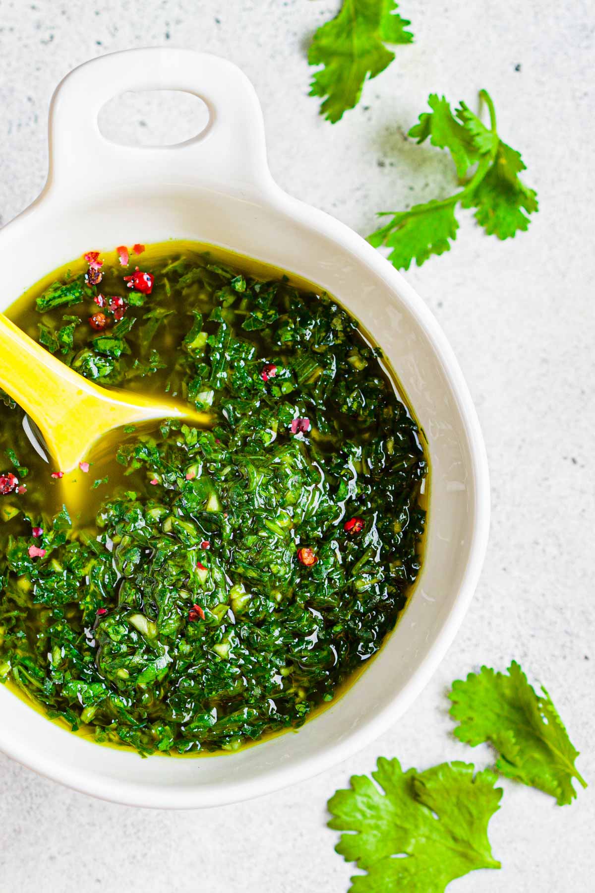 chimichurris sauce in a white bowl with a yellow spoon