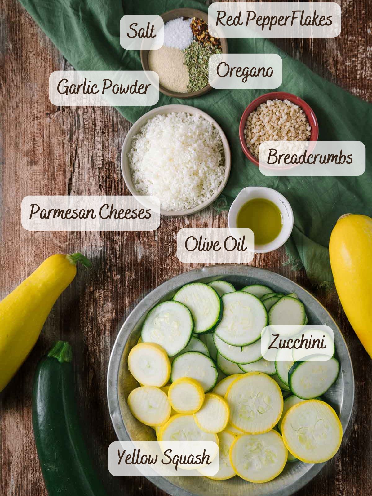 A bowl of sliced zucchini and yellow squash for Roasted Zucchini and Squash, surrounded by bowls of grated parmesan cheese, olive oil, breadcrumbs, garlic powder, salt, oregano, and red pepper flakes.