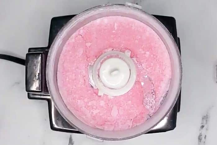 A food processor filled with pink crushed ice sits atop a marble surface, reminiscent of the vibrant hues of Valentine puppy chow.