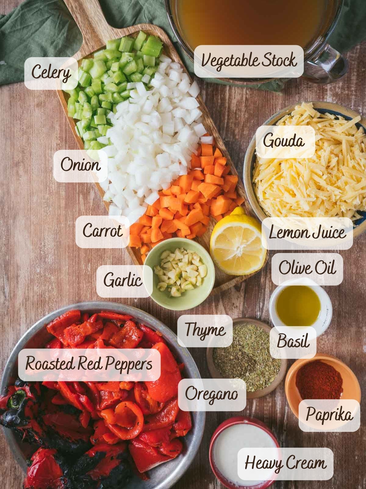 Chopped celery, onion, carrot, garlic, roasted red peppers, gouda, lemon juice, olive oil, vegetable stock, herbs, and cream ready to create a delicious roasted red pepper soup with gouda on the table.