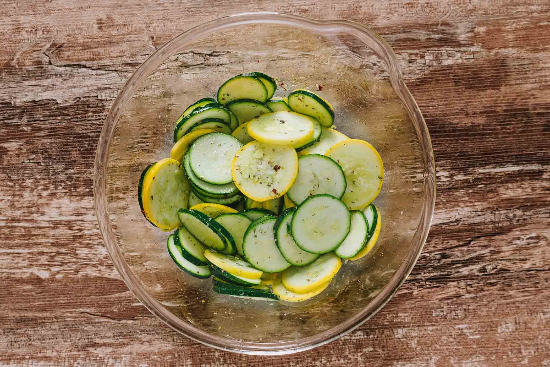 seasoning zucchini and yellow squash in a bowl with olive oil and spices.