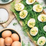 deviled eggs on bed or dill with basket of eggs to the side.