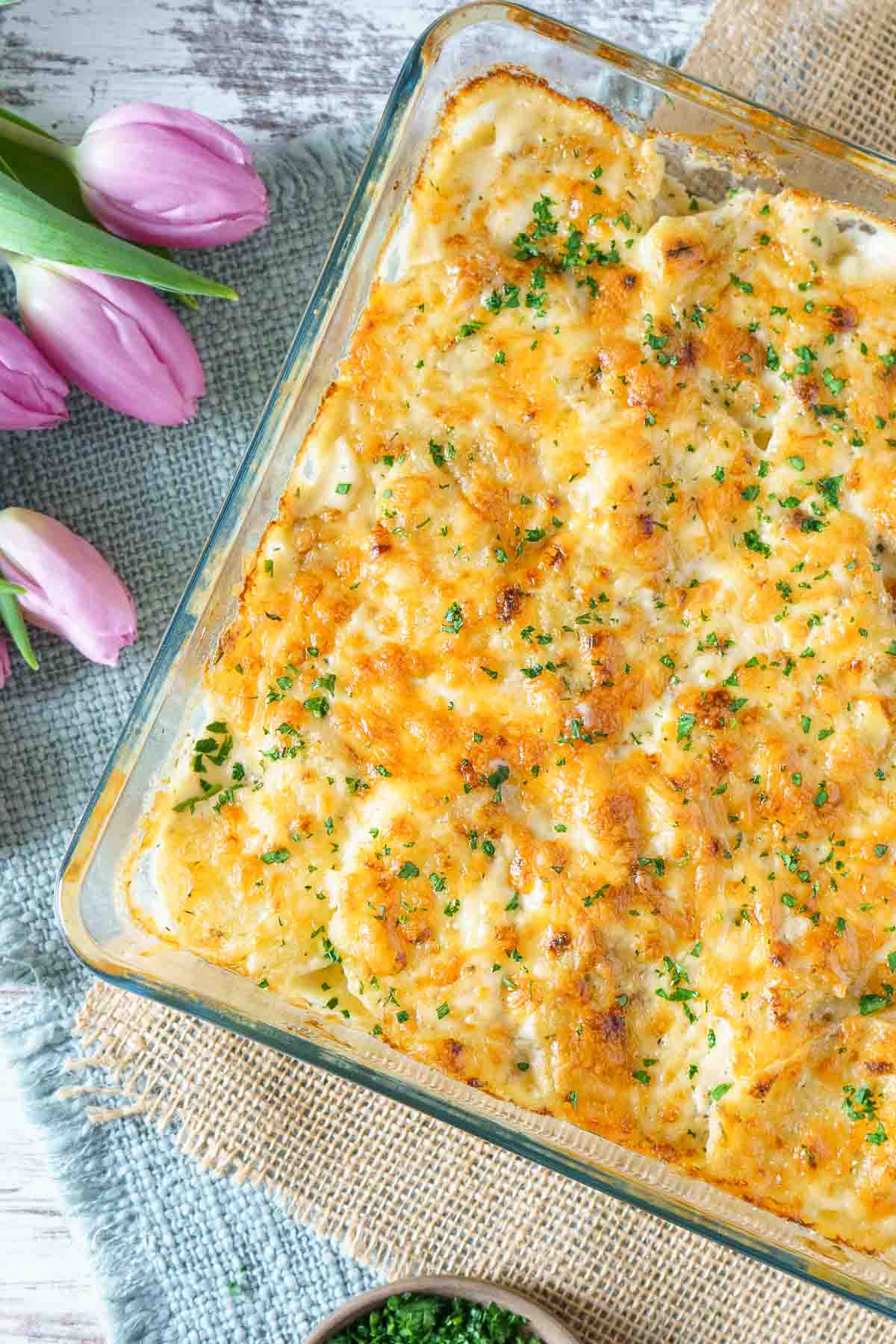 scalloped potatoes in a casserole dish with tulips to the side. 