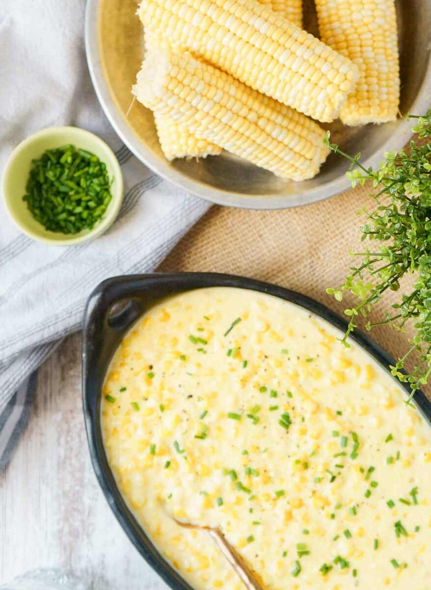 creamed corn in serving dish with fresh corn cobs to the side.