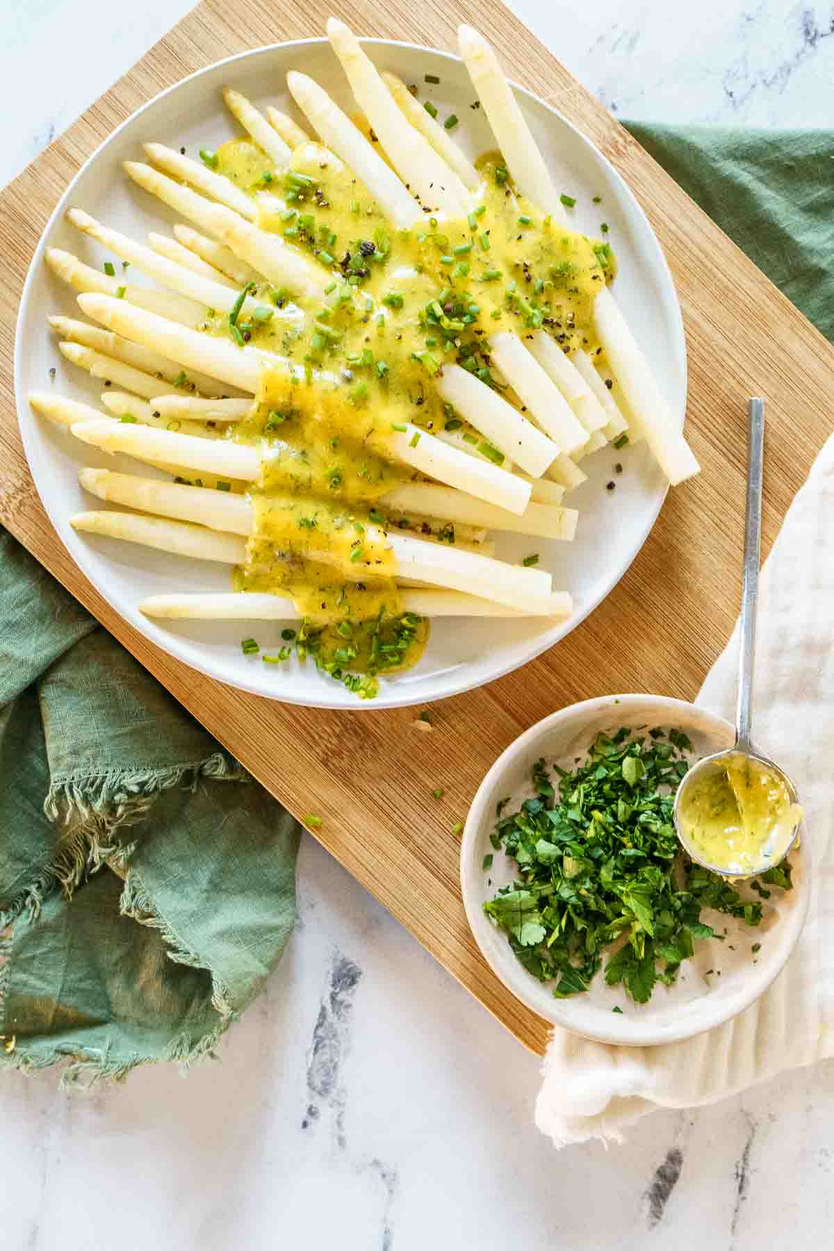 white asparagus on plate with butter sauce and side of herbs.