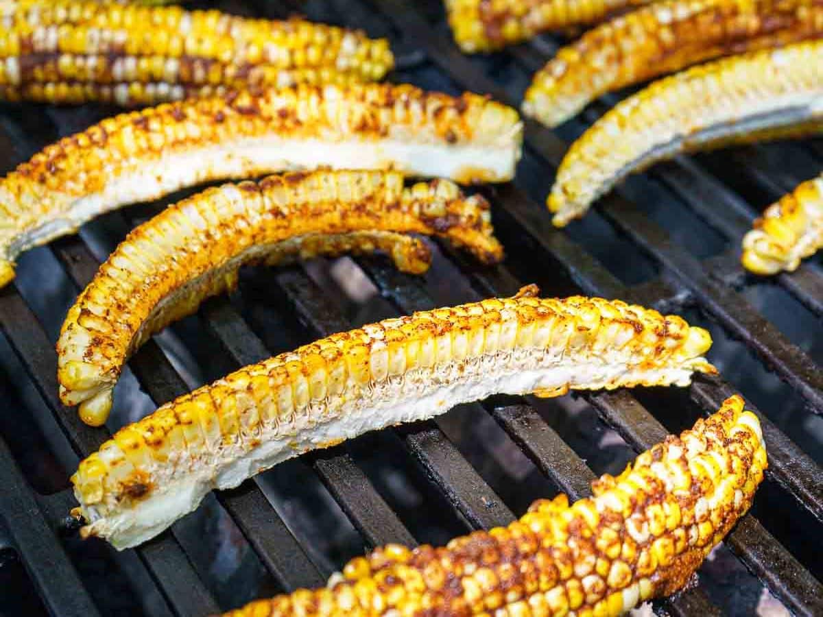Several quartered ears of corn, inspired by a corn ribs recipe, are grilling on a barbecue, showing char marks and seasoned surfaces.