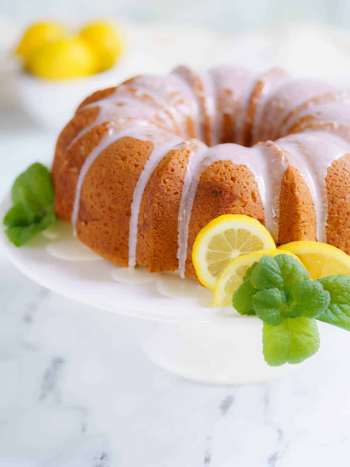 lemon drizzle cake on white stand with lemon wedges and mint