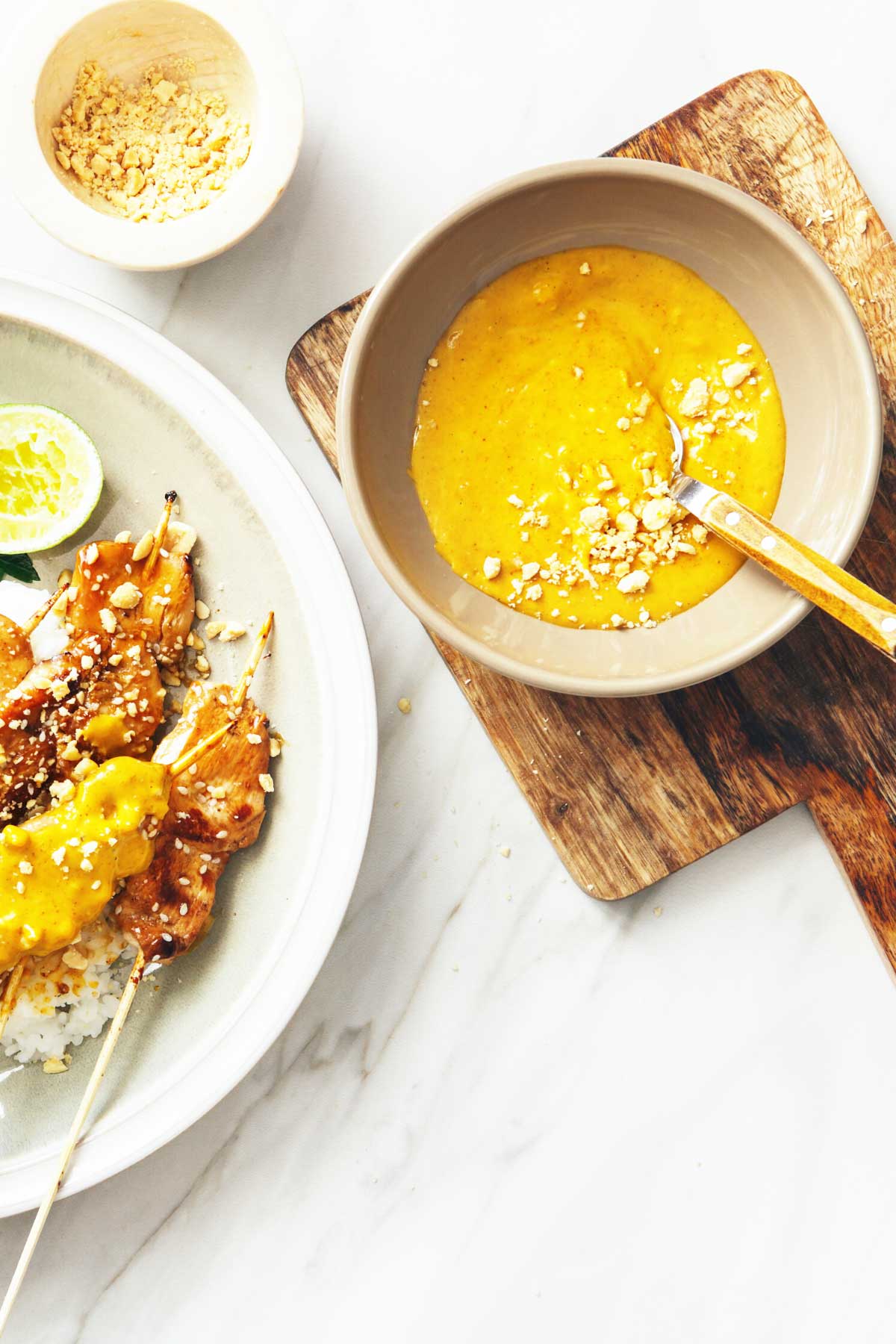 peanut sauce in a serving dish on a cutting board next to chicken satay