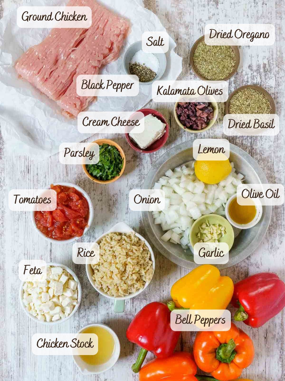 A variety of labeled ingredients on a white surface, perfect for making ground chicken stuffed peppers-featuring ground chicken, vegetables, herbs, seasonings, cheeses, rice, olives, and chicken stock.