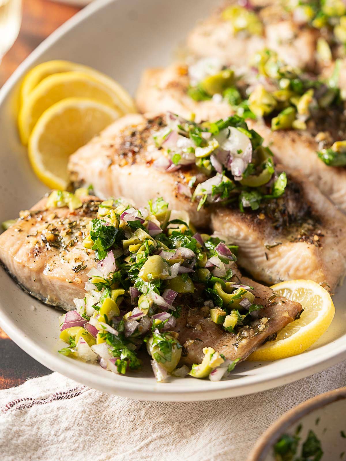 Grilled fish fillets topped with a chopped olive and herb garnish, served with lemon slices on a white plate—perfect for those who love a twist on the classic baked mahi mahi recipe.