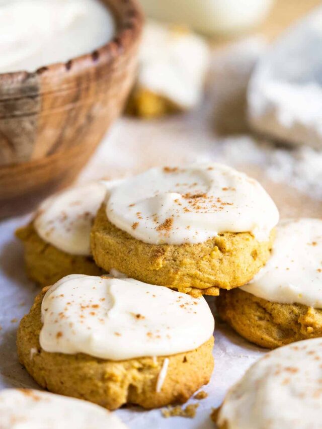 Pumpkin cookies on a counter with a bowl of icing.