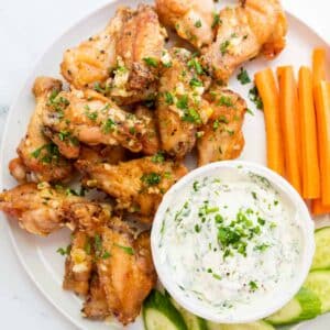Garlic butter chicken wings on a plate with carrots and ranch.