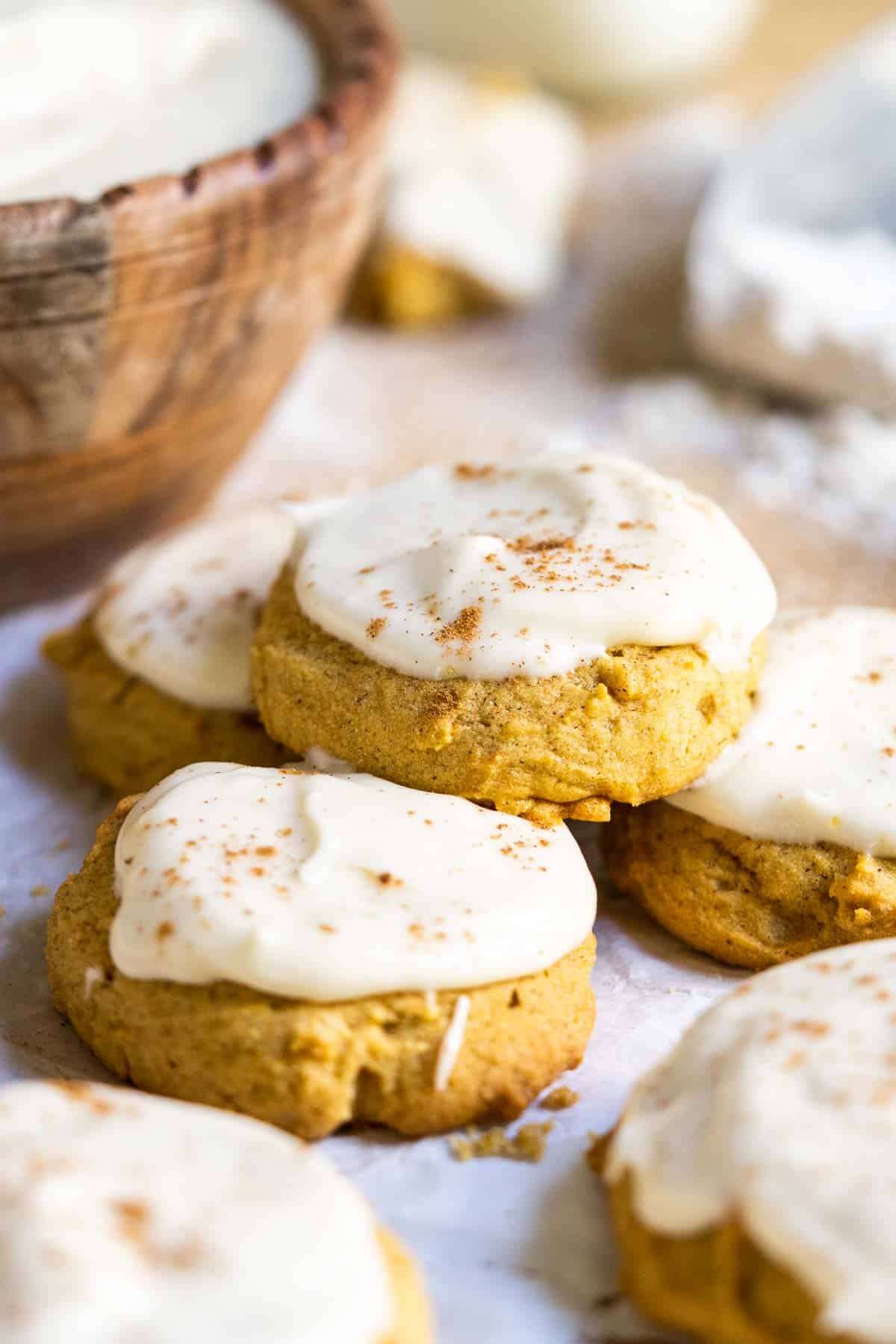 Pumpkin cookies on a counter with a bowl of icing.