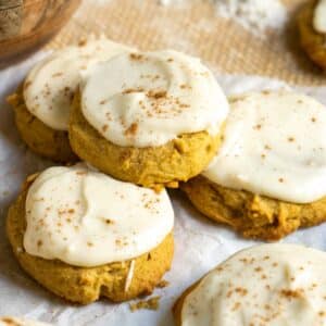 Pumpkin cookies with icing and spices stacked on counter.