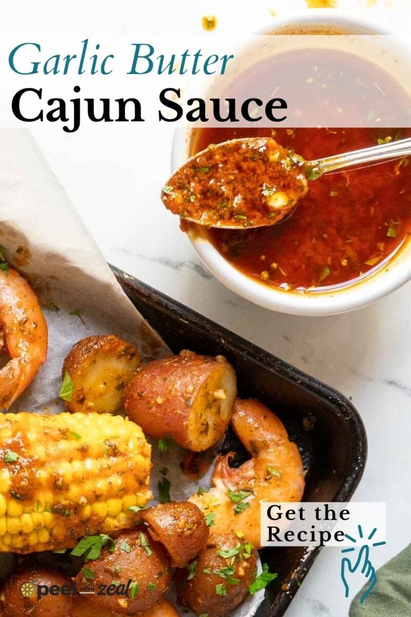 A bowl of cajun garlic butter sauce with a spoon beside a tray of shrimp, corn, and potatoes; text reads "Garlic Butter Cajun Sauce" and "Get the Recipe.