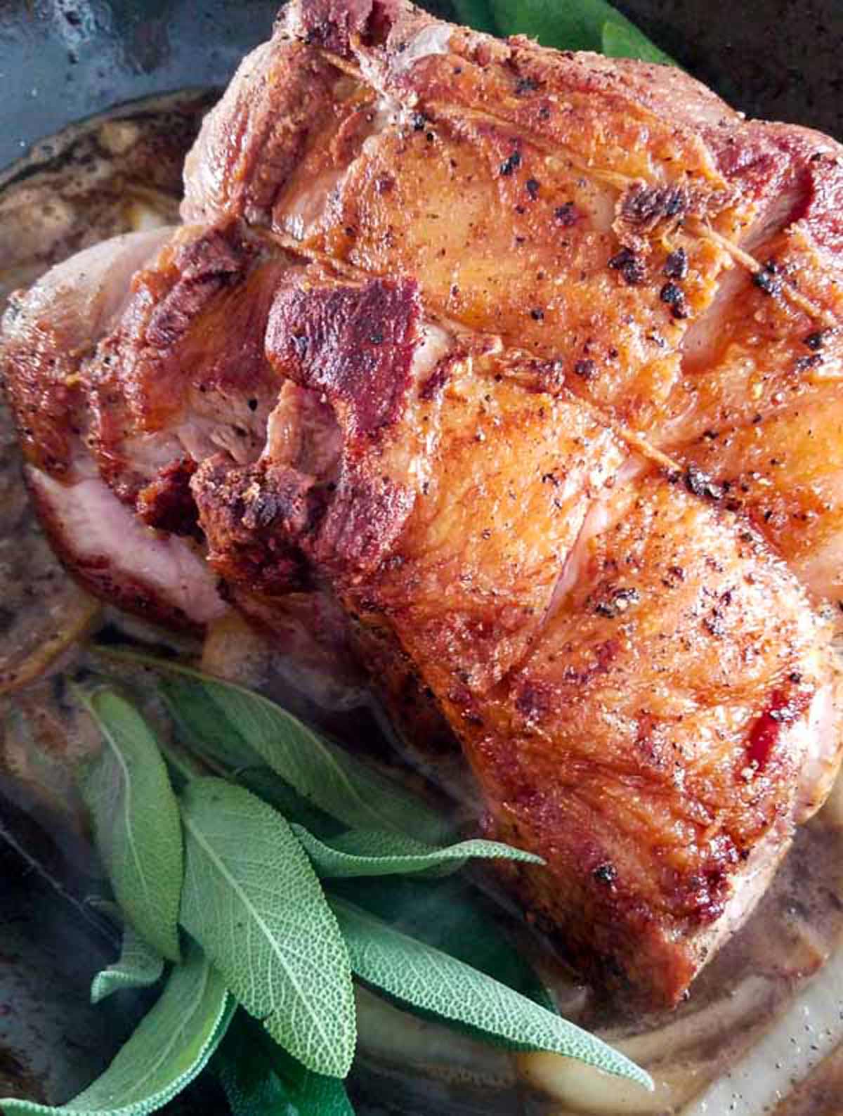 Pork shoulder in a roasting pan with fresh sage.