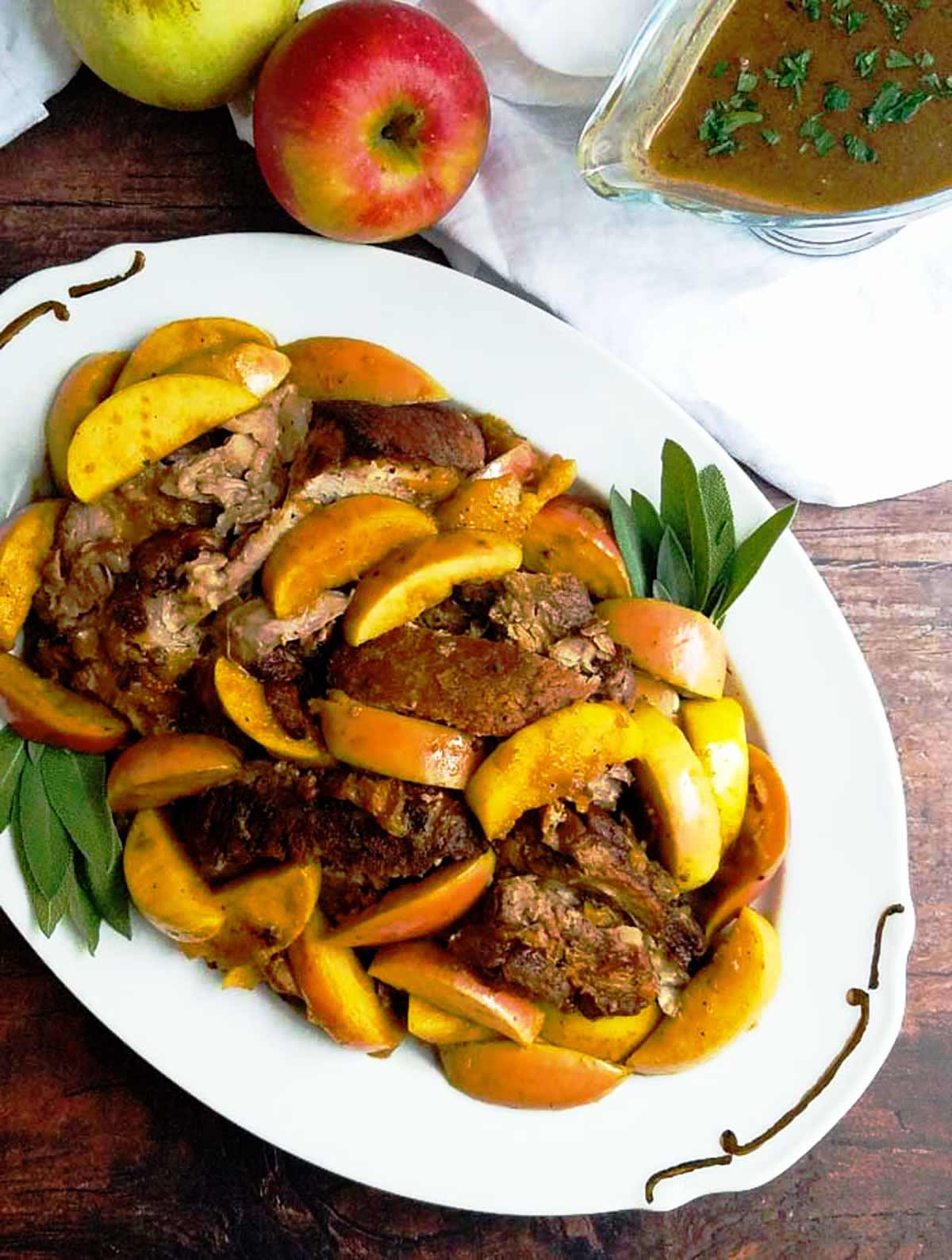 Pork shoulder on a platter with apples and pan sauce.