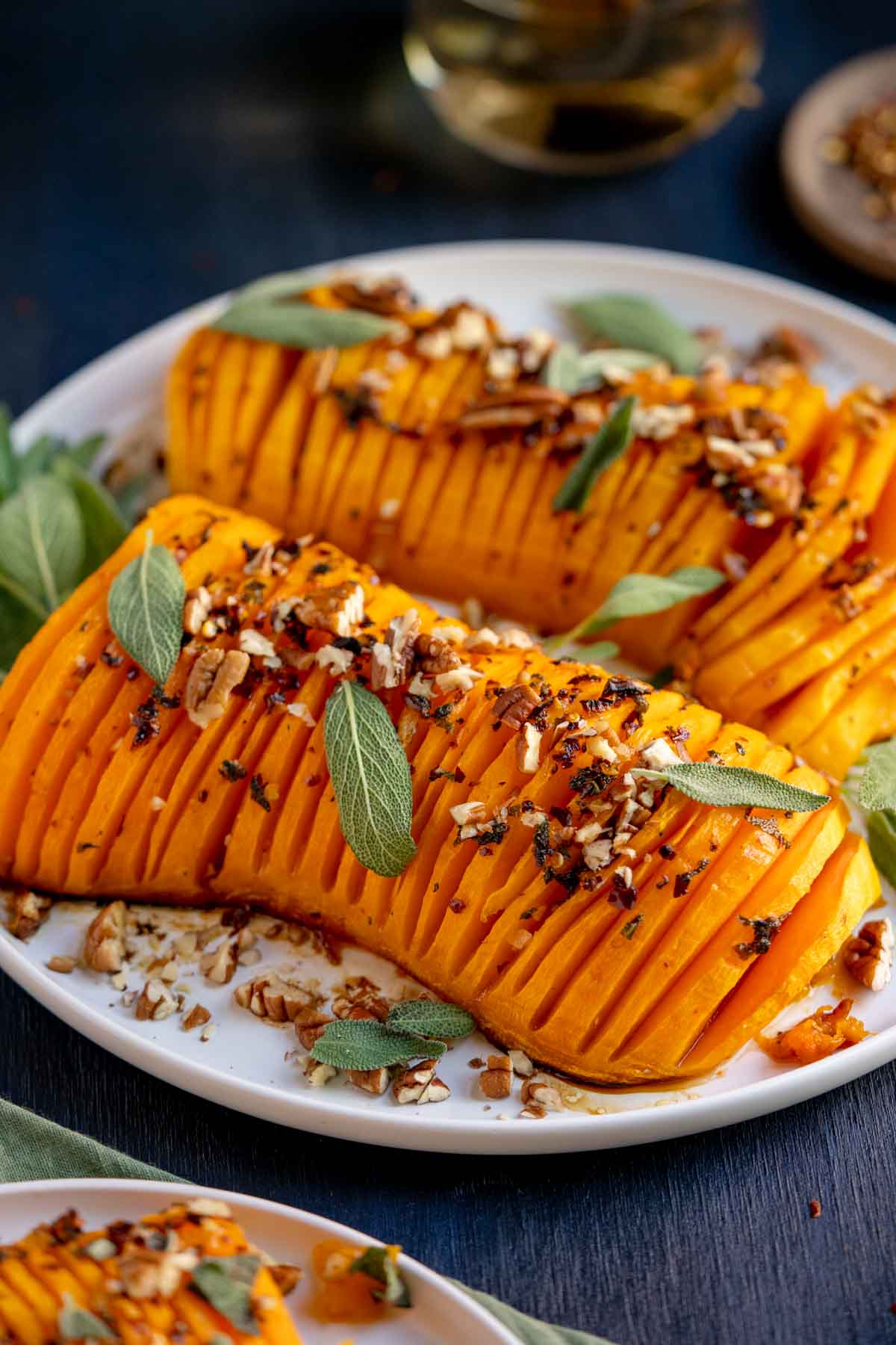 Hasselback style squash on a white plate with sage leaves.