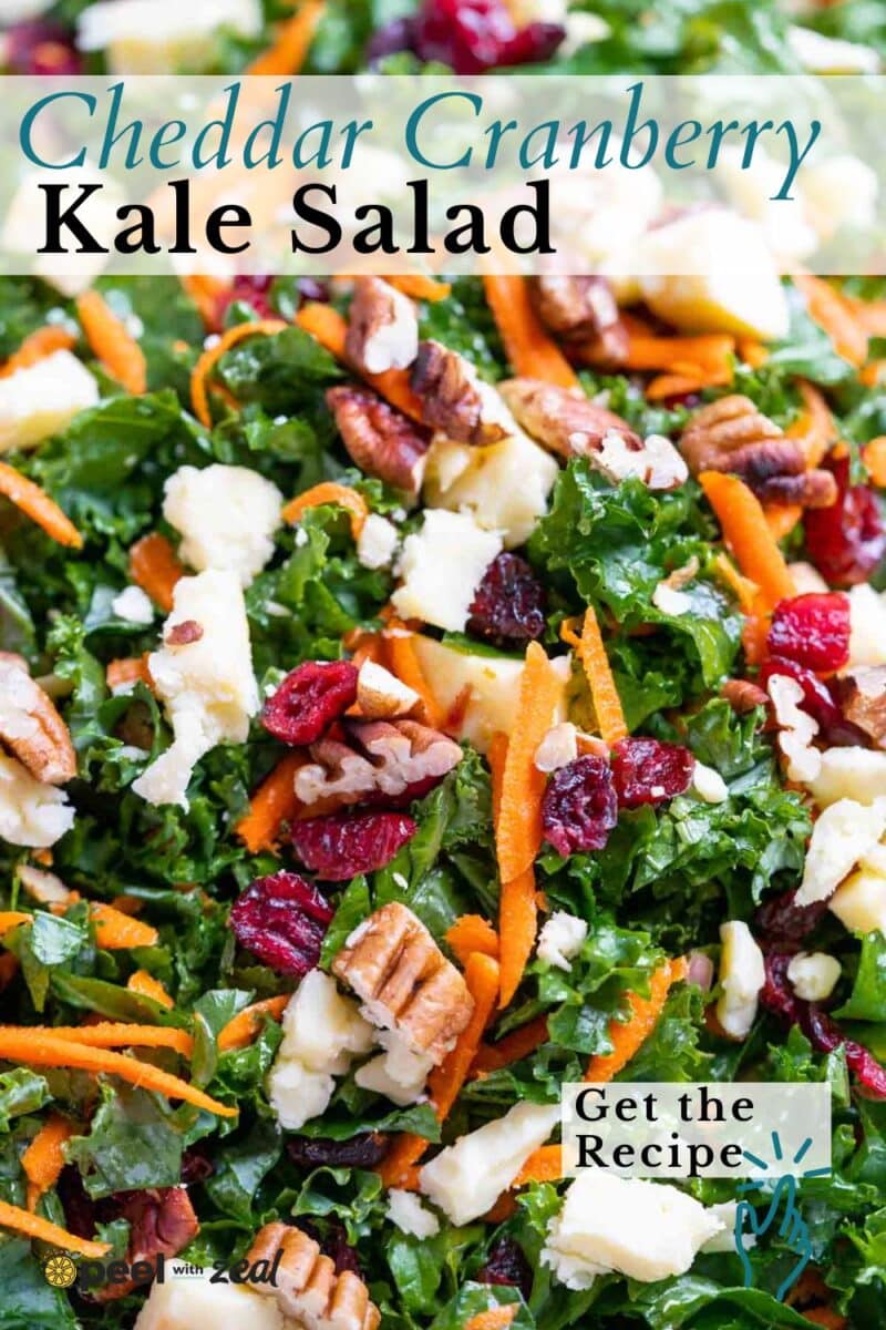 Close-up of a Kale Salad with Cranberries, shredded cheddar, pecans, and carrot strips. Text reads “Cheddar Cranberry Kale Salad” and “Get the Recipe.”.