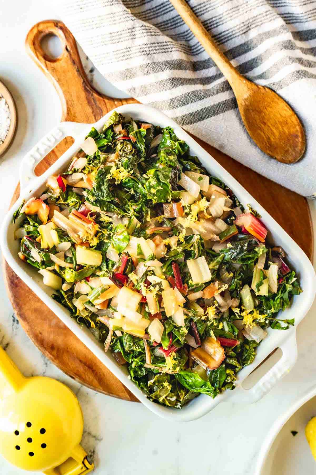 Sauteed rainbow chard in a white dish with lemon zest and a wooden spoon.