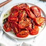 Roasted tomatoes on a white plate with a fork and napkin.