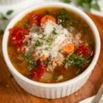Bowl of soup with vegetables and ground turkey in broth with cheese and fresh herbs on top.