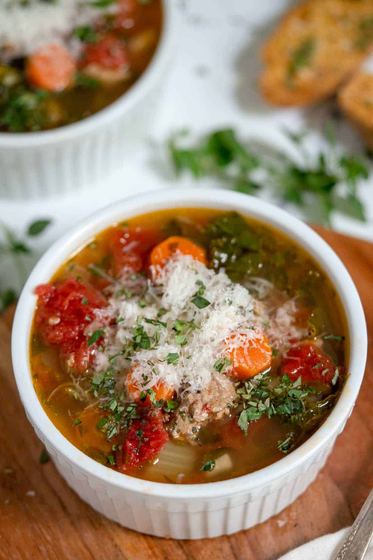 Bowl of soup with vegetables and ground turkey in broth with cheese and fresh herbs on top.
